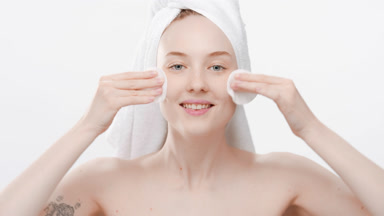 Beautiful young woman touches cheeks using cotton pads smiling