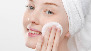 European young woman touches cheek using cotton pad smiling wide