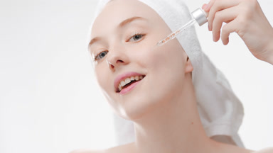 Woman with a towel on hair drips serum from dropper on cheek