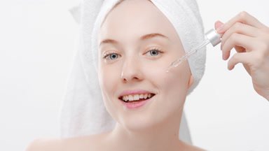 Young woman drips skincare serum from dropper on cheek smiling