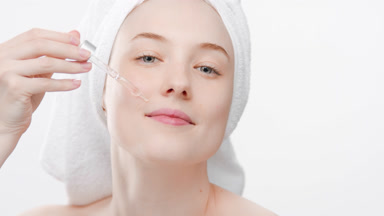 Young woman drips face care serum from dropper on face smiling