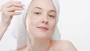 Woman drips nourishing serum from dropper on cheek smiling wide