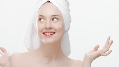 Woman applies cream on face from hand tapping and smiling wide