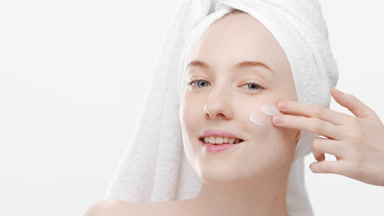 Woman applies face care cream on cheek turning head and smiling