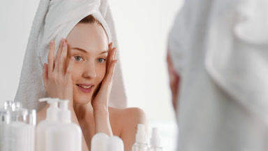 Caucasian woman touches face smiling wide in front of mirror
