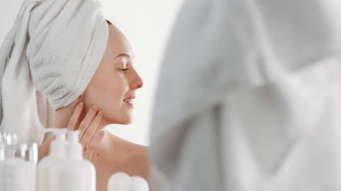 Slim young woman turns head and touches neck in front of mirror