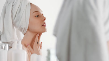 Fit young woman touches neck smiling wide in front of the mirror