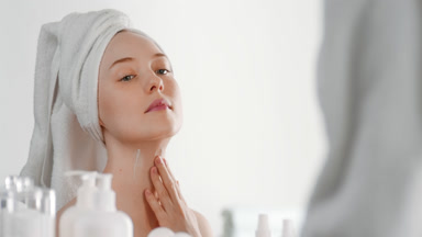 Slim young woman applies nourishing cream on neck smiling wide