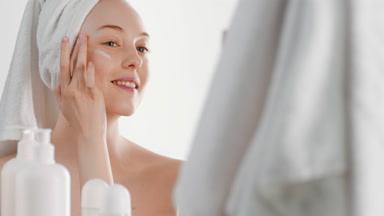 Attractive European young woman applies face care cream on cheek