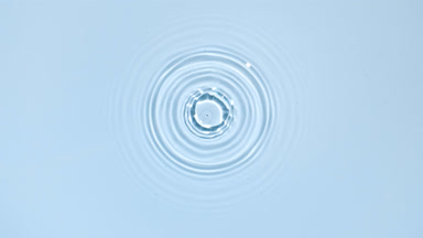 White drop falls down creating circles on water surface