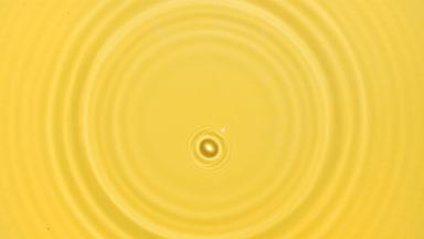 Drop falls on water surface creating rings on yellow background