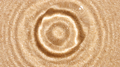 Water drop makes ripples on water surface against brown sugar