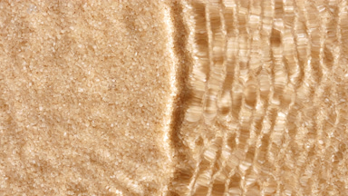 Wave makes ripples and splashes on water surface over cane sugar