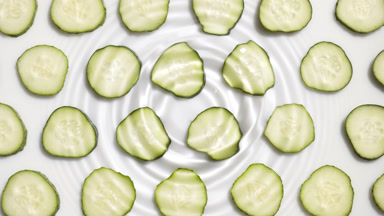 Drop falls on water creating rings on cucumber slices background