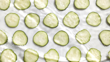 Water waves crossing and splashing over cucumber slices white bg