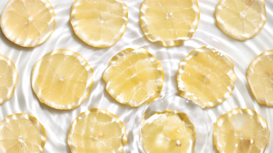 Drops falls in water making rings over lemon slices on white bg