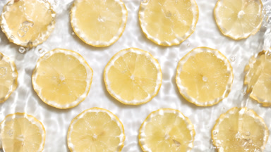 Water splashing and making ripples over lemon slices on white bg