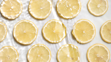 Water waves crossing and splashing over lemon slices on white bg