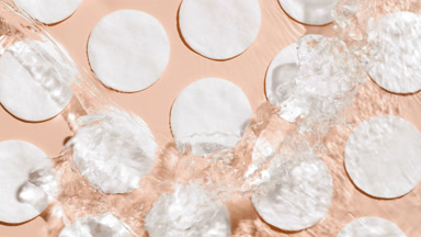 Water splashing and making ripples over cotton pads on beige bg