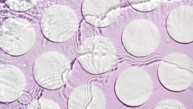 Water splashing and making ripples over cotton pads on purple bg