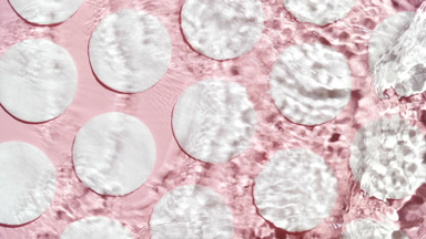 Water making splashes and ripples over cotton pads on pink bg