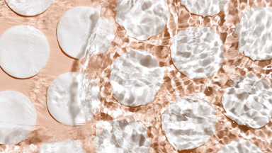 Water making splashes and ripples over cotton pads on beige bg