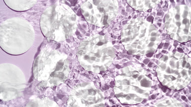 Water making splashes and ripples over cotton pads on purple