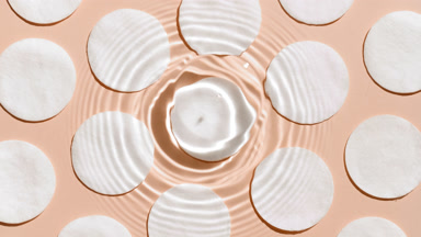 Water drop makes ripples on surface over cotton pads on beige bg