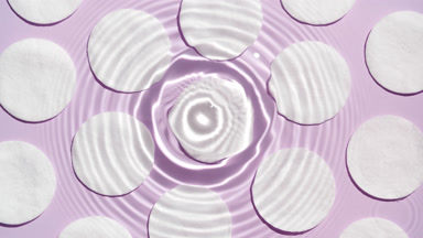 Water drop makes rings on surface over cotton pads on purple bg
