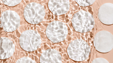 Wave makes water ripples surface over cotton pads on beige bg