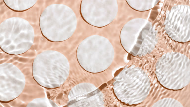 Wave makes ripples on water surface over cotton pads on beige bg