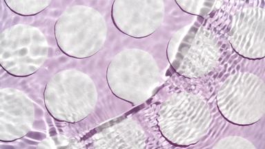 Wave makes ripples on water surface over cotton pads on purple