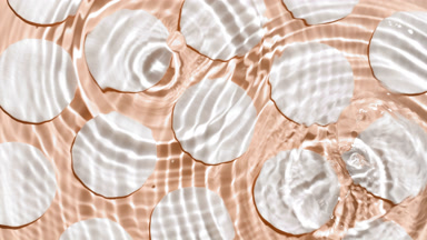 Drops falling in water making rings over cotton pads on beige bg
