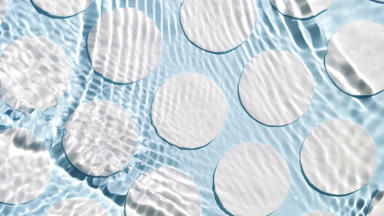 Poured water splashes and makes ripples over cotton pads on blue