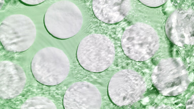 Drop makes ripples on water surface over cotton pads on green bg
