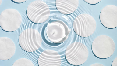 Drop makes water rings on water surface over cotton pads on blue
