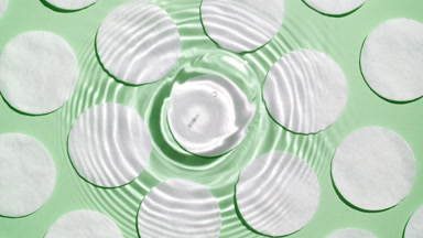 Drops falling in water making rings over cotton pads on green bg