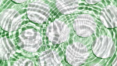 Wave makes ripples on water surface over cotton pads on green bg