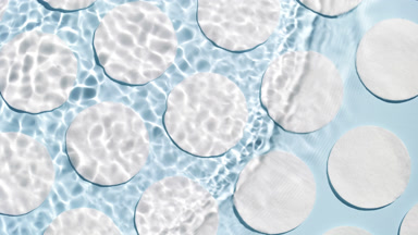 Wave splashing on water surface over cotton pads on blue bg