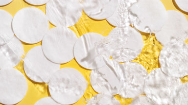 Water splashing and makes ripples over cotton pads on yellow bg