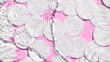 Water splashes and makes ripples over cotton pads on pink bg