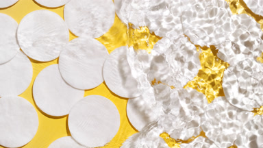 Water makes splashes and ripples over cotton pads on yellow bg