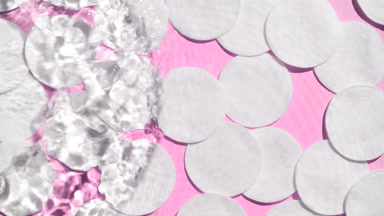 Water makes splashes and ripples over cotton pads on pink bg