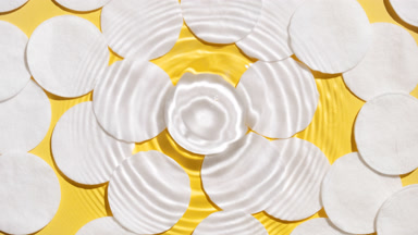 Drop makes rings on water surface over cotton pads on yellow bg