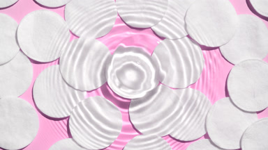 Drop makes ripples on water surface over cotton pads on pink bg