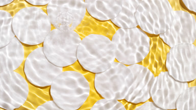 Drops falling in water making rings over cotton pads on yellow