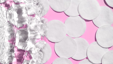 Wave splashing on water surface over cotton pads on pink bg