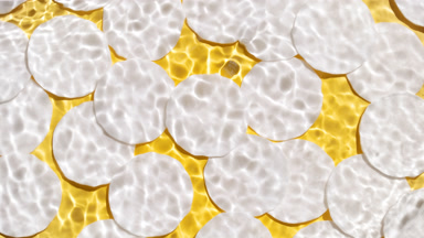 Wave makes ripples on water surface over cotton pads on yellow