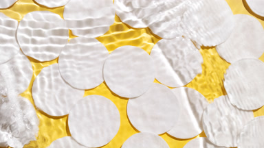 Water waves crossing and splashing against cotton pads yellow bg