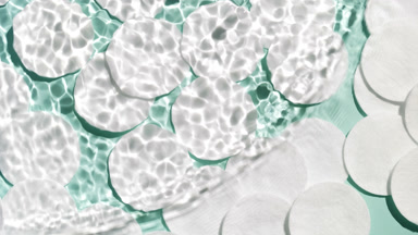 Wave makes water ripples over cotton pads on green background